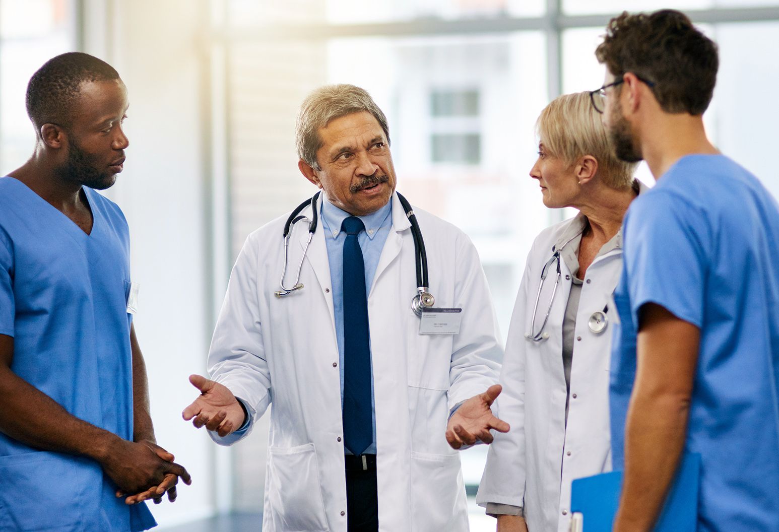 A group of four doctors have a conversation in a hospital hallway.