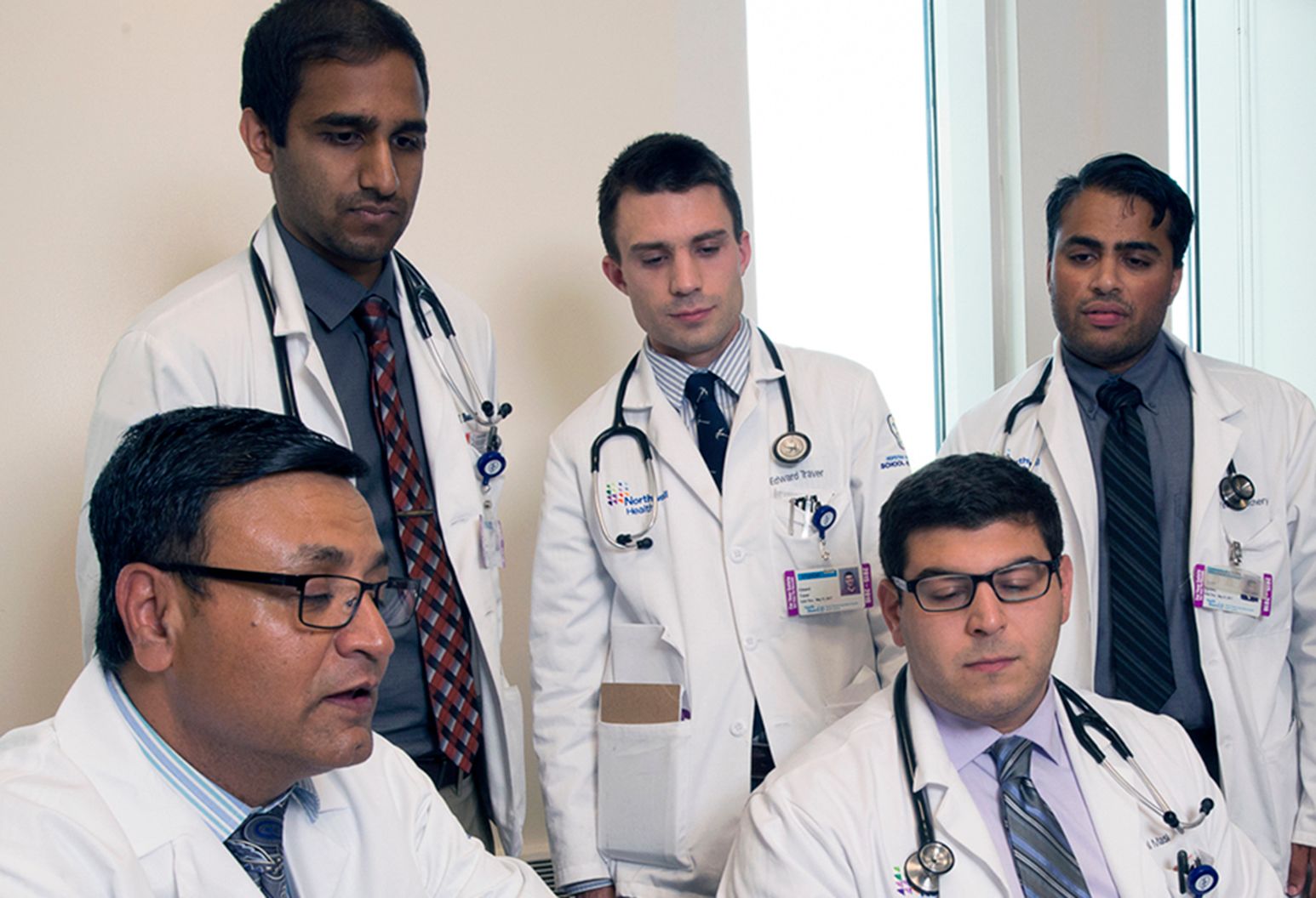 Five physician residents, all men, looking at a computer screen.