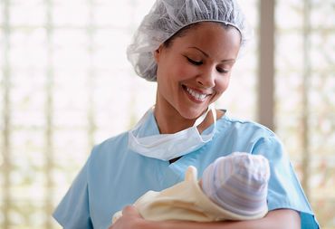 Female physician in blue scrubs, cradling and gazing down at new born baby