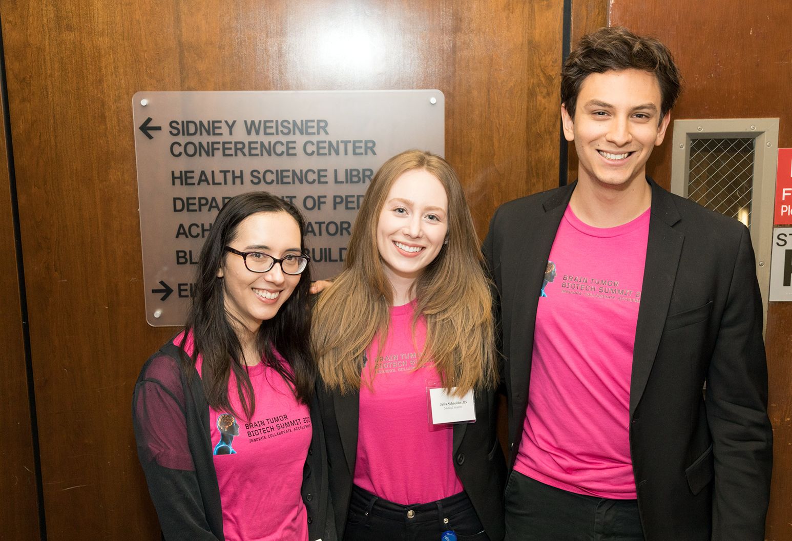 Three young medical students who are wearing matching pink shirt pose for a group photograph