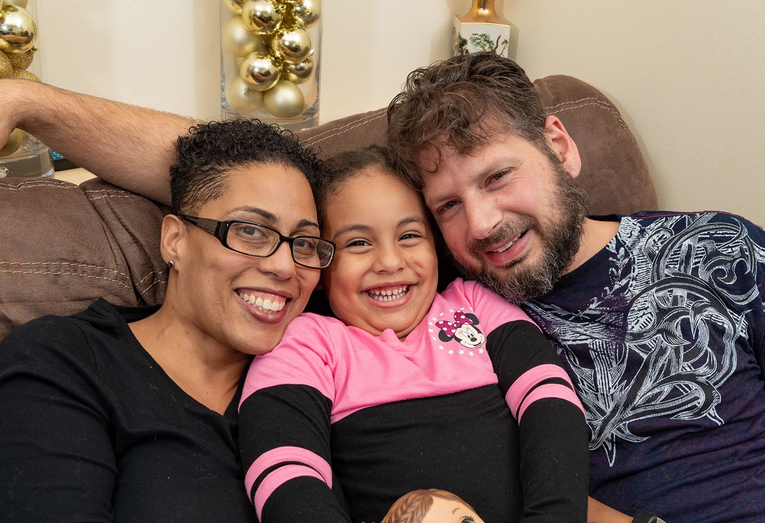 A female patient smiles with her husband and daughter on the couch in their home.