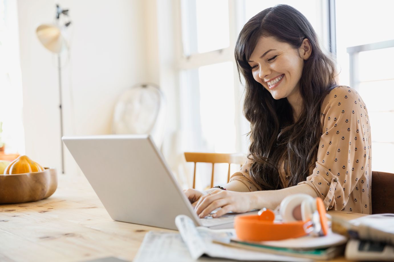 woman sitting at table, smiling and looking at laptop