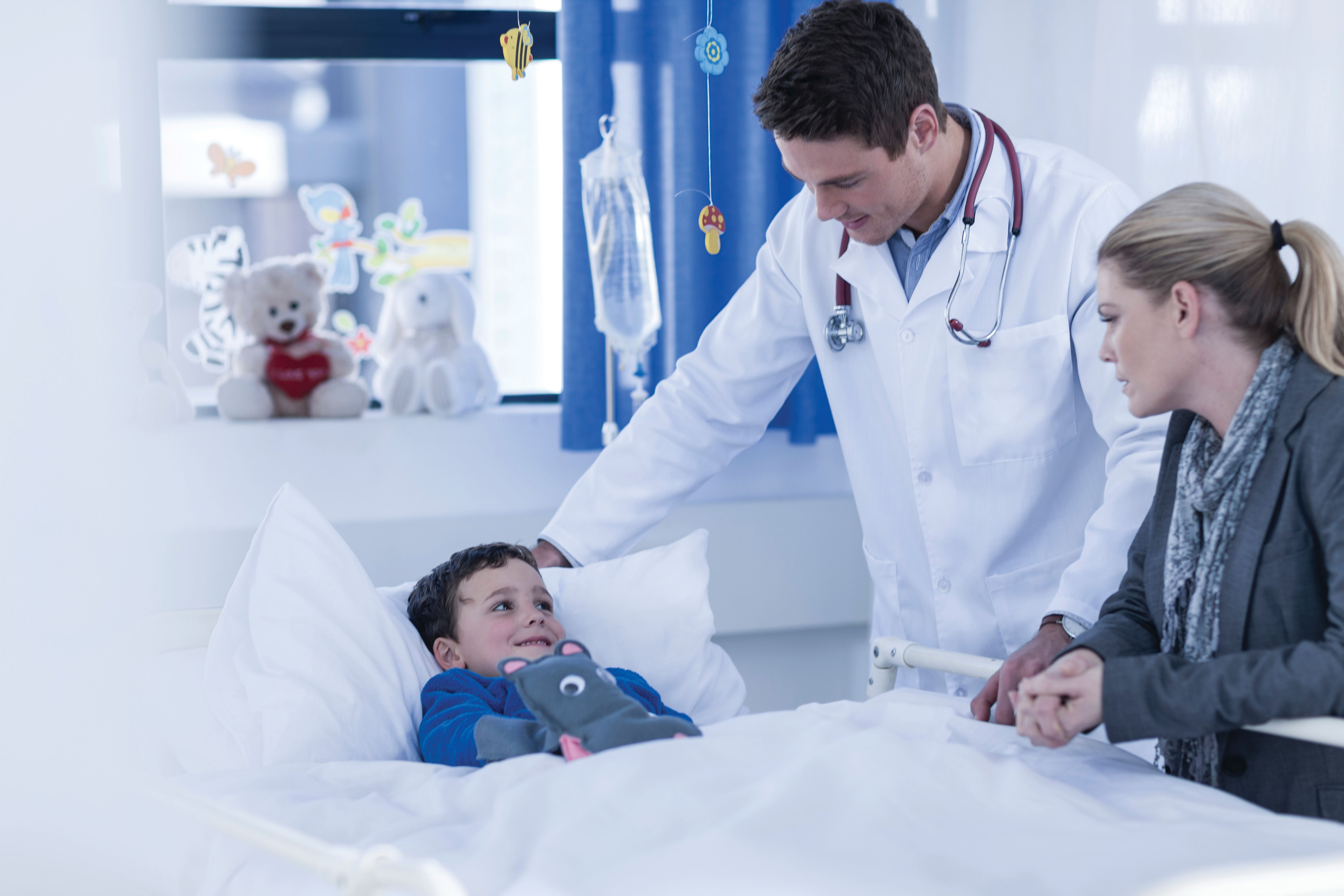 A doctor and mother watch over a boy in a hospital bed.