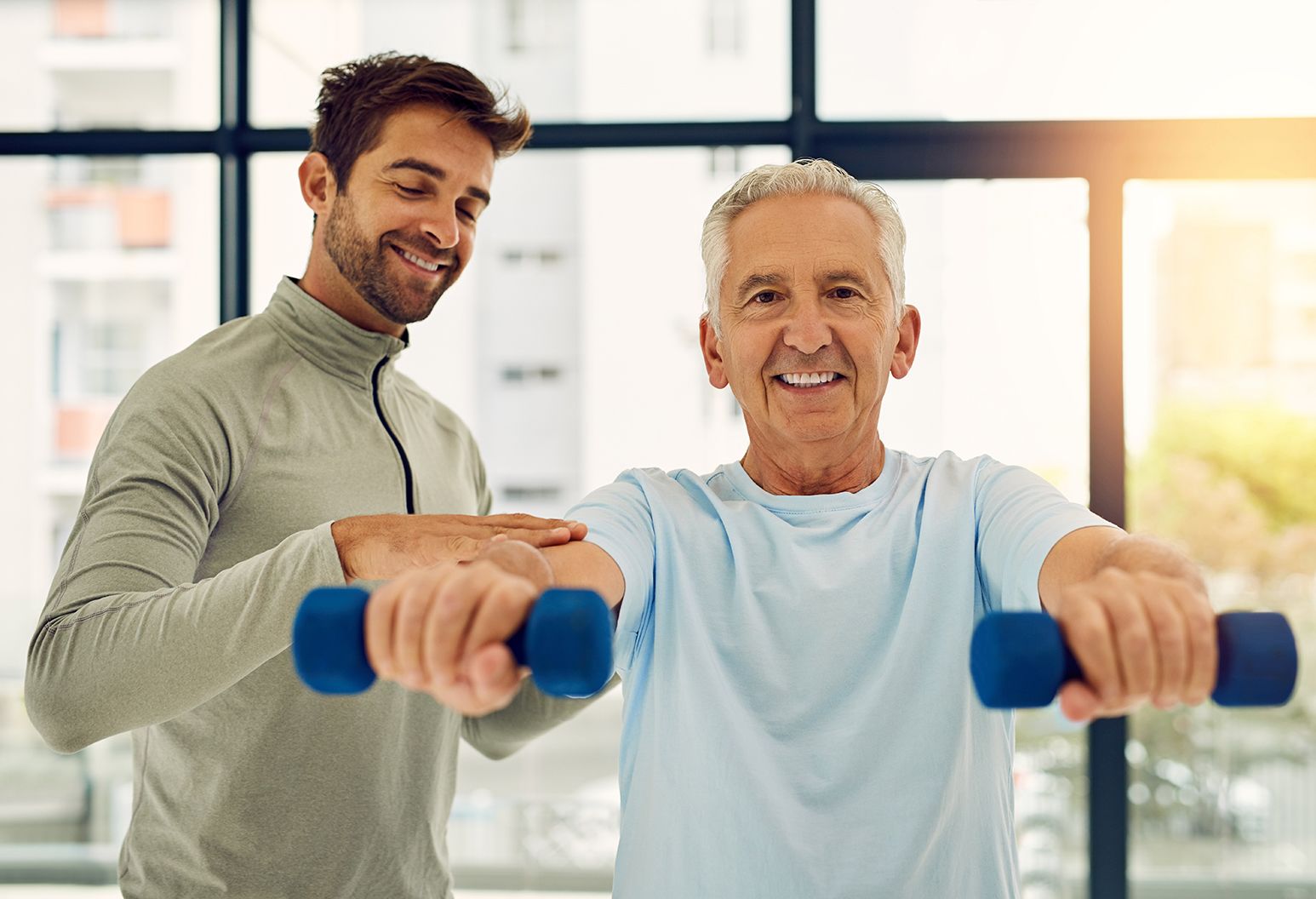 Portrait of a friendly physiotherapist helping his senior patient work out with weights