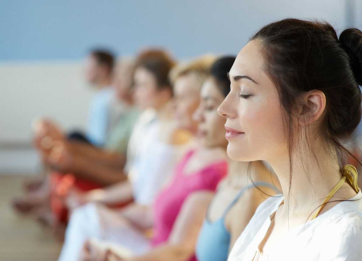 Row of woman with their eyes closed, doing yoga