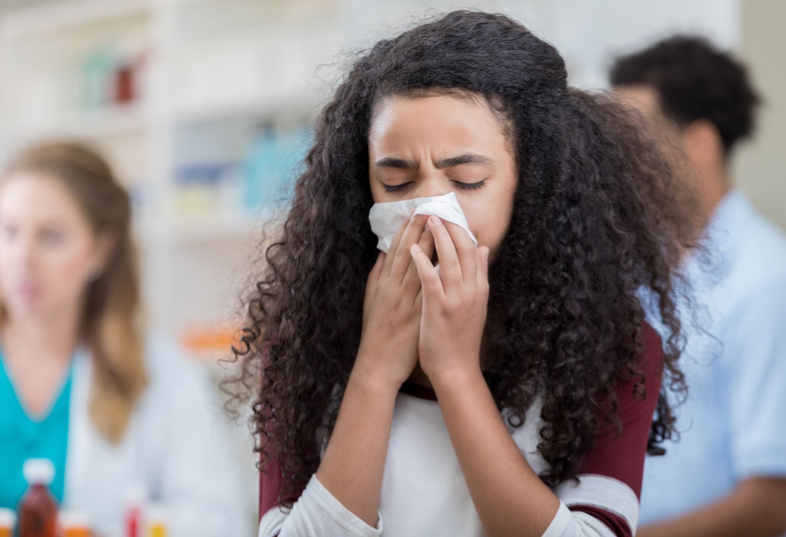 A young woman with brown hair blows her nose into a white tissue