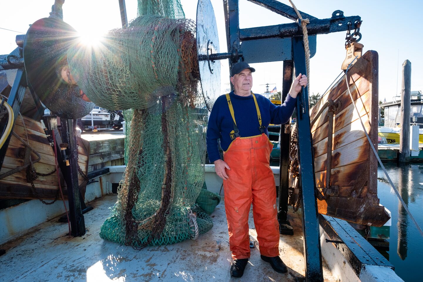 An older man in fishing gear on a commercial fishing boat looking out to the horizon on a sunny day.