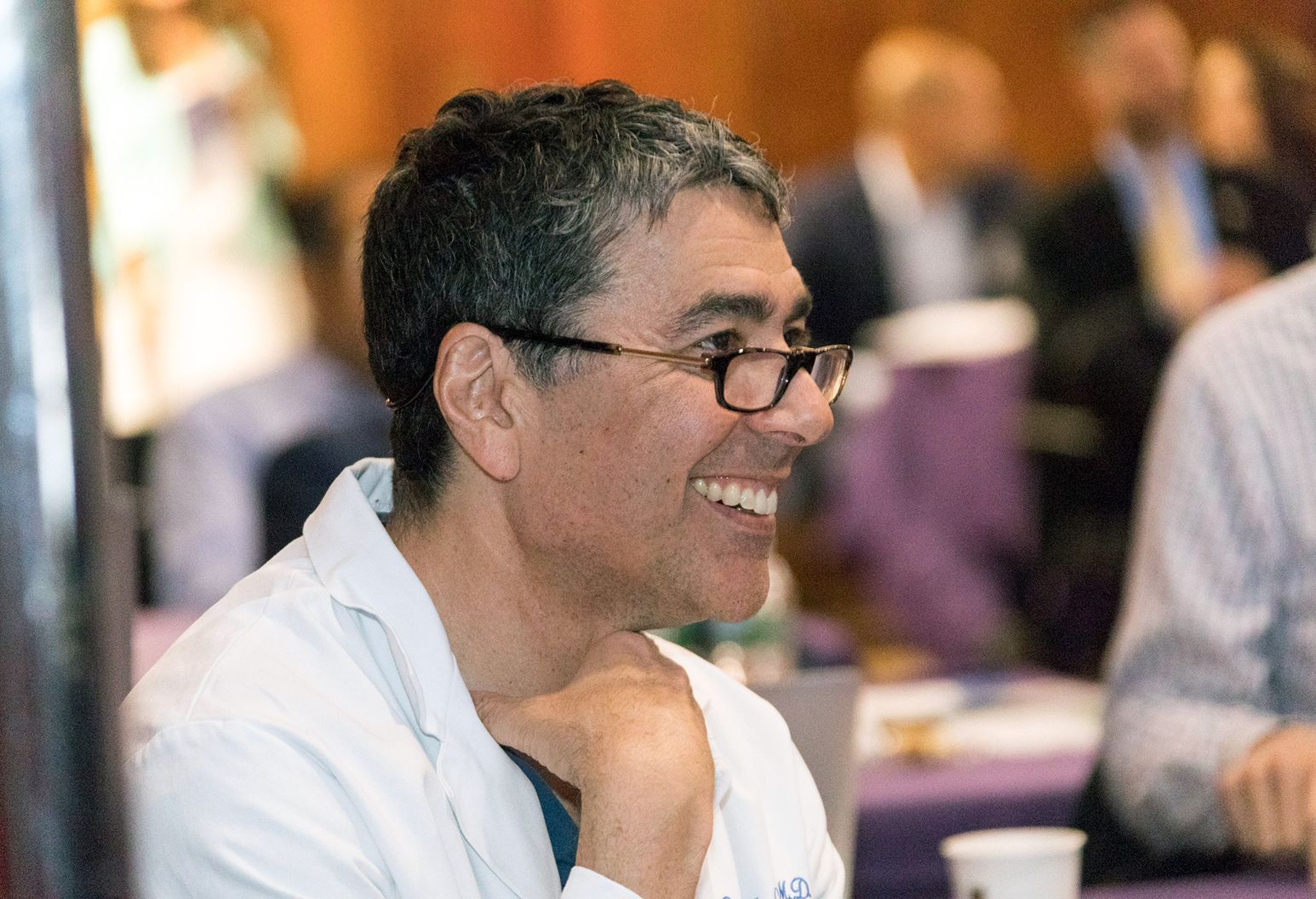 Close up photograph of a middle aged male doctor smiling while he is watching a presentation