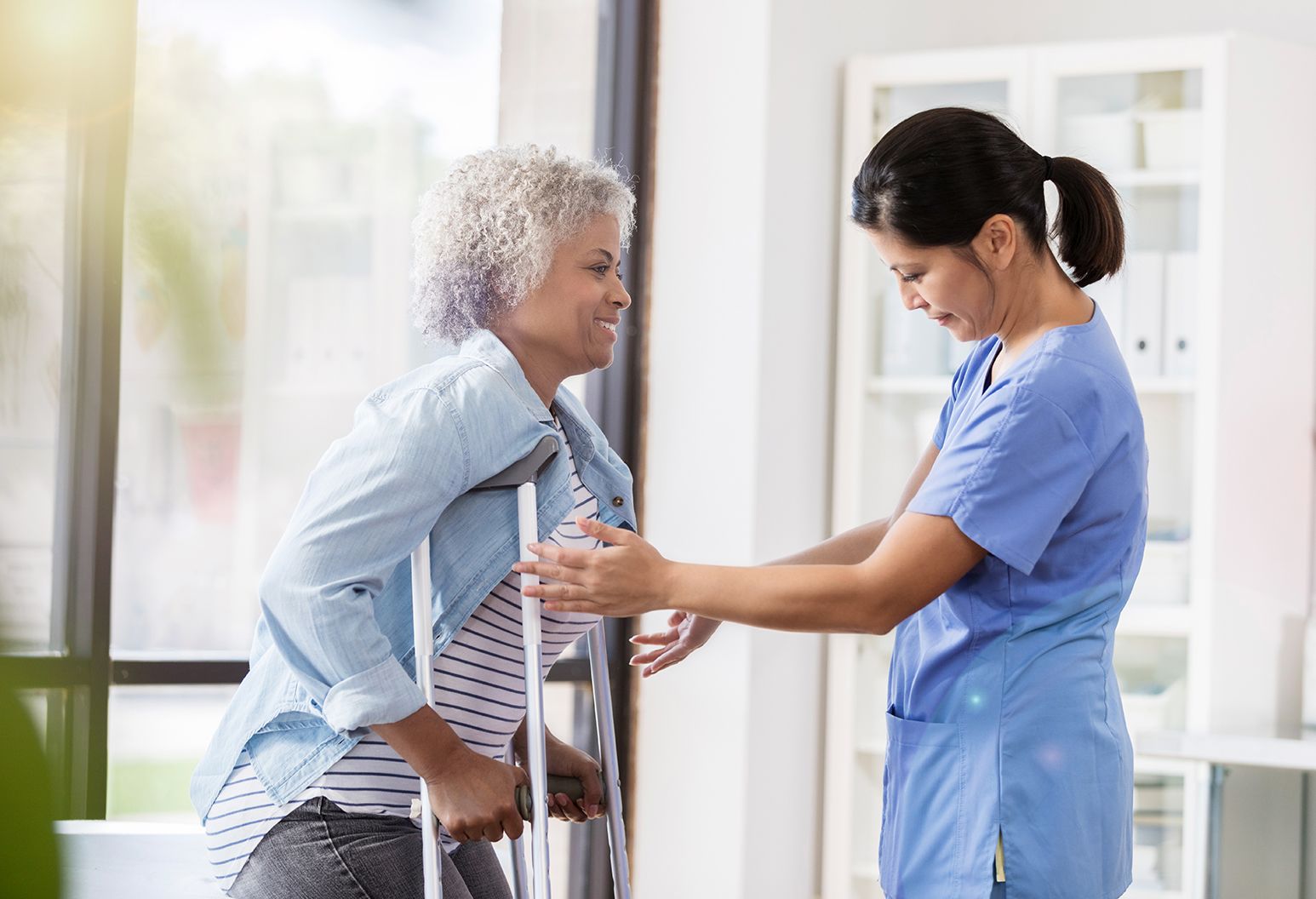 Senior woman on crutches works with a caring female physical therapist during her recovery process.
