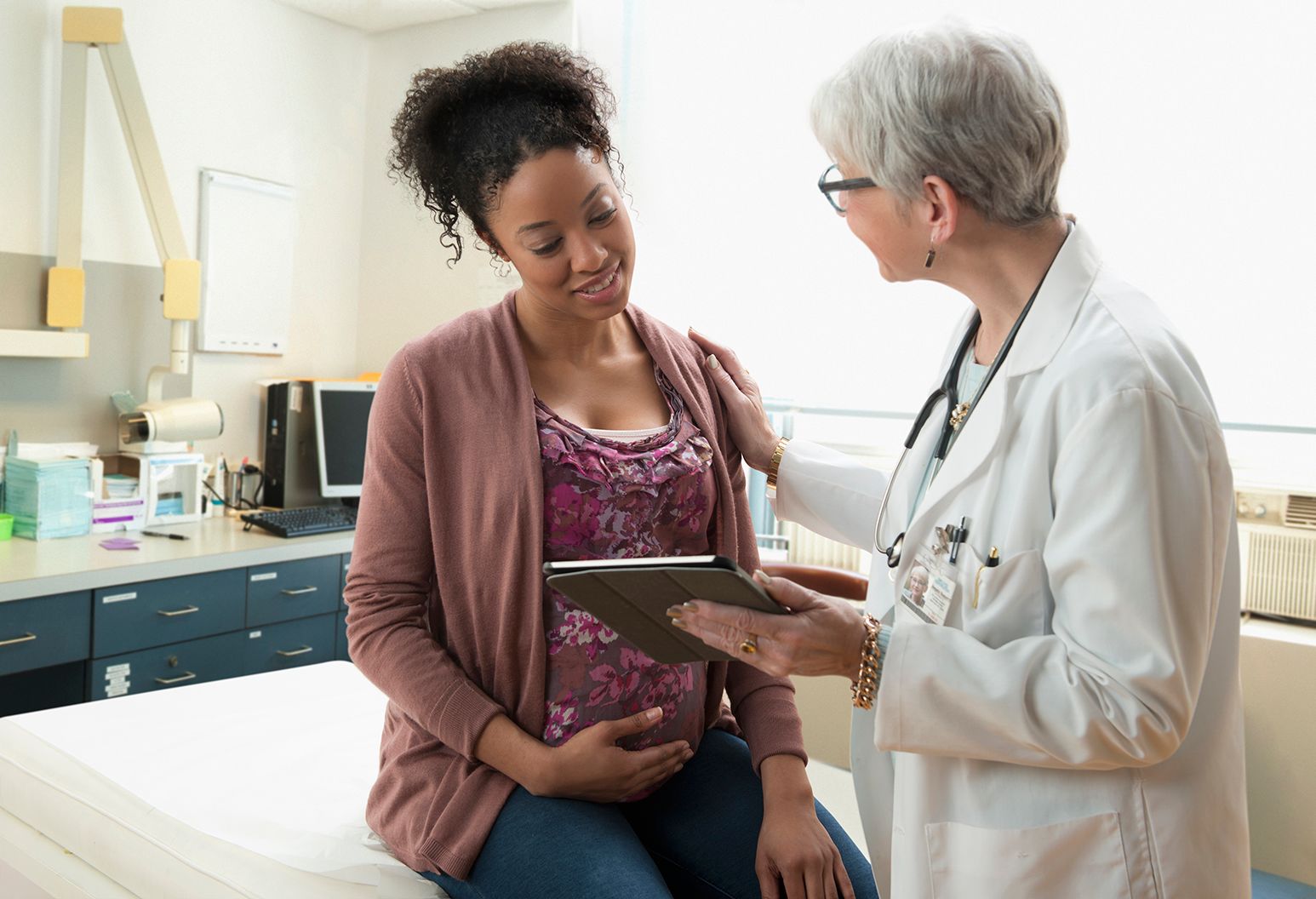 Gynecologist with digital tablet comforting pregnant patient