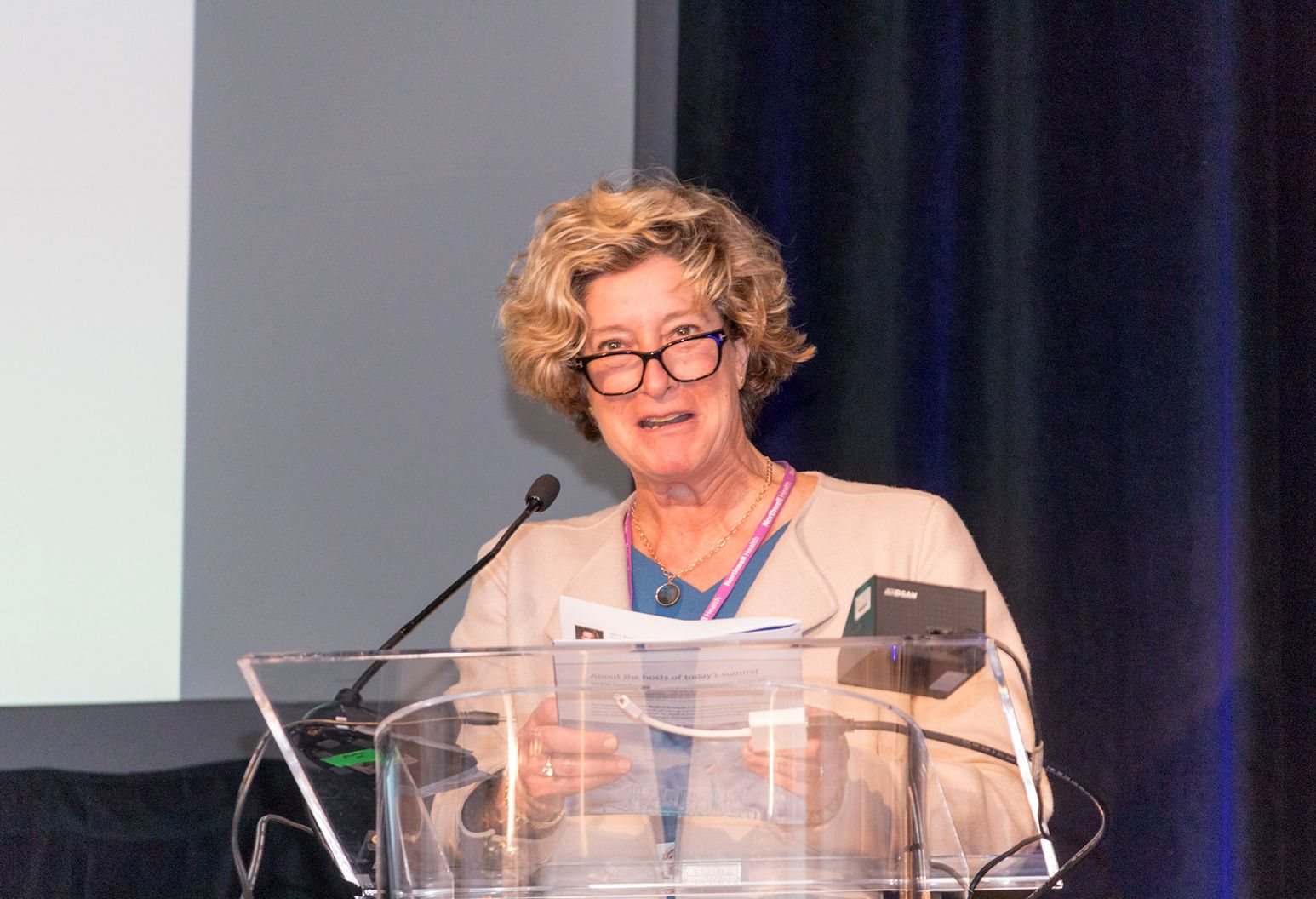 Middle aged woman stands behind a podium on stage at a conference