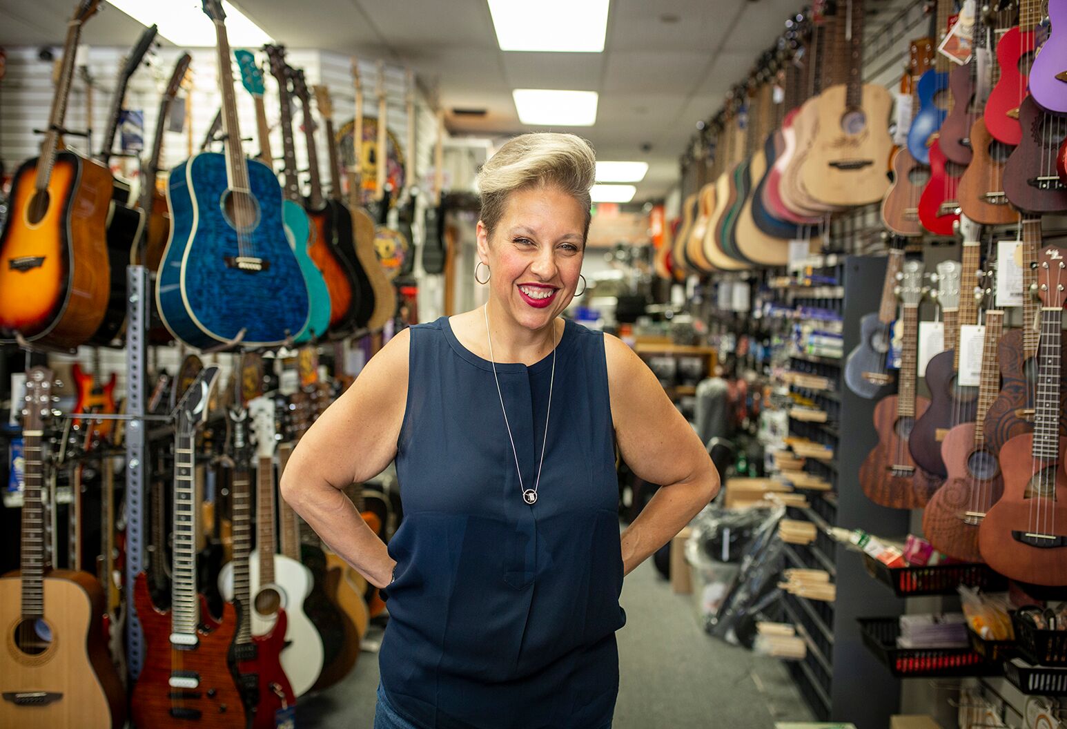 Woman in her 50s with short blond hair and navy top in a guitar store.