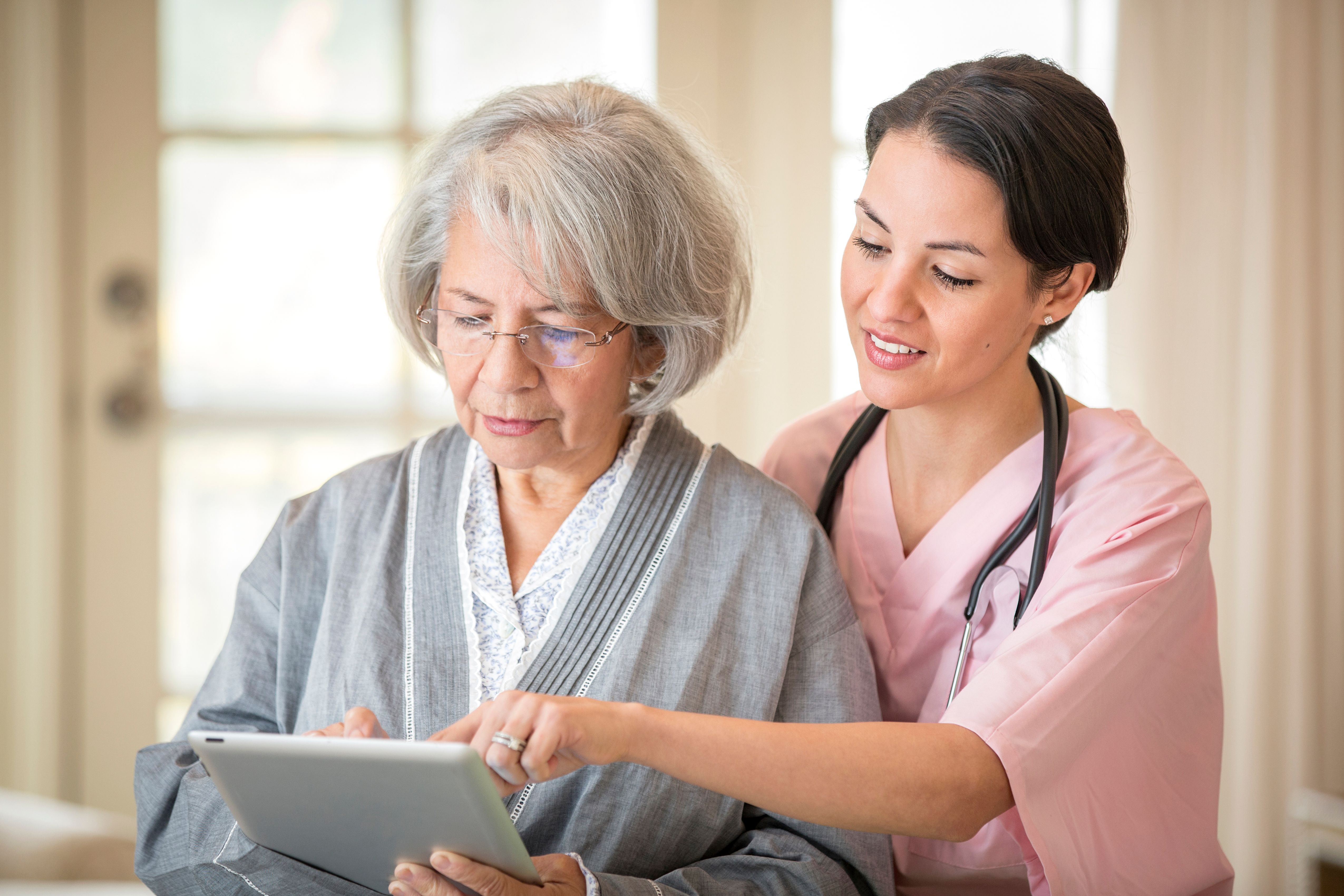 A female nurse shows an elderly woman how to use a tablet.