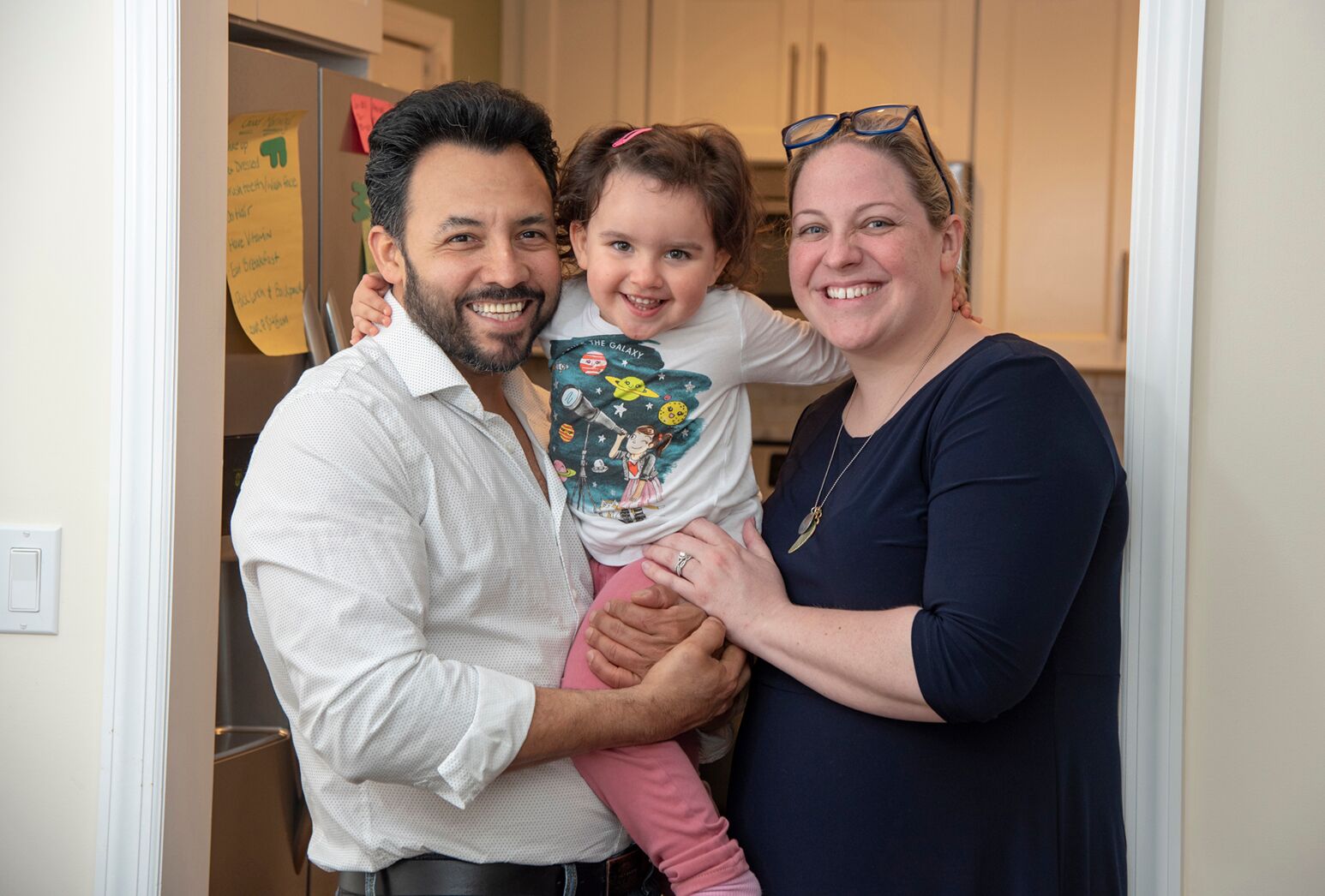 Father, mother and toddler pose for a picture in their home.