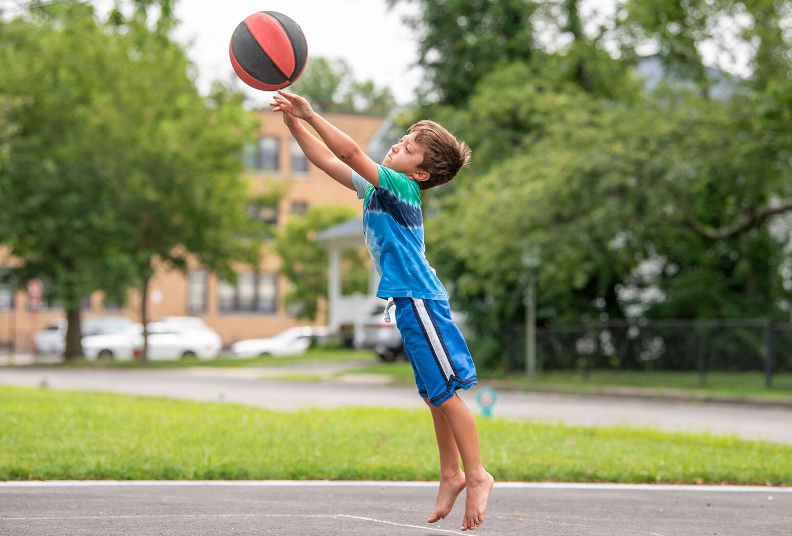 Barefoot little boy in blue shorts and top shooting a basketball.