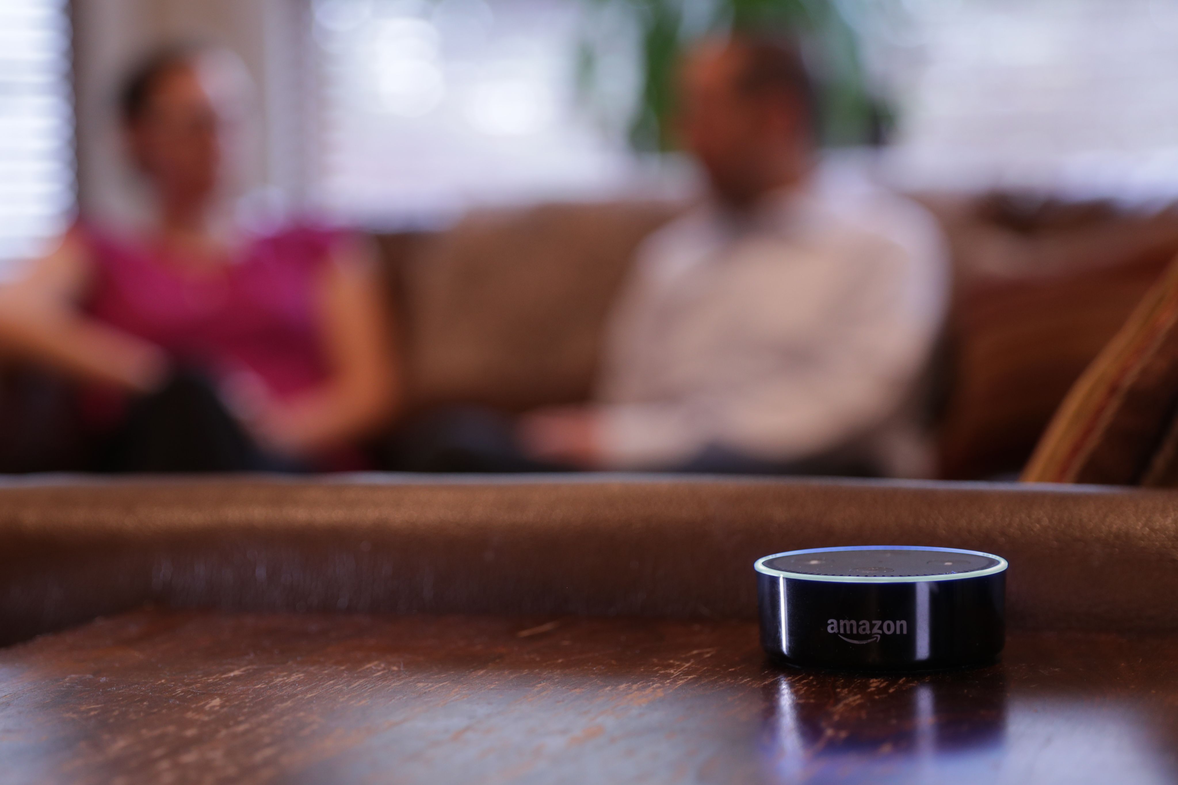 Amazon echo on table in house's living room, two people sitting in background
