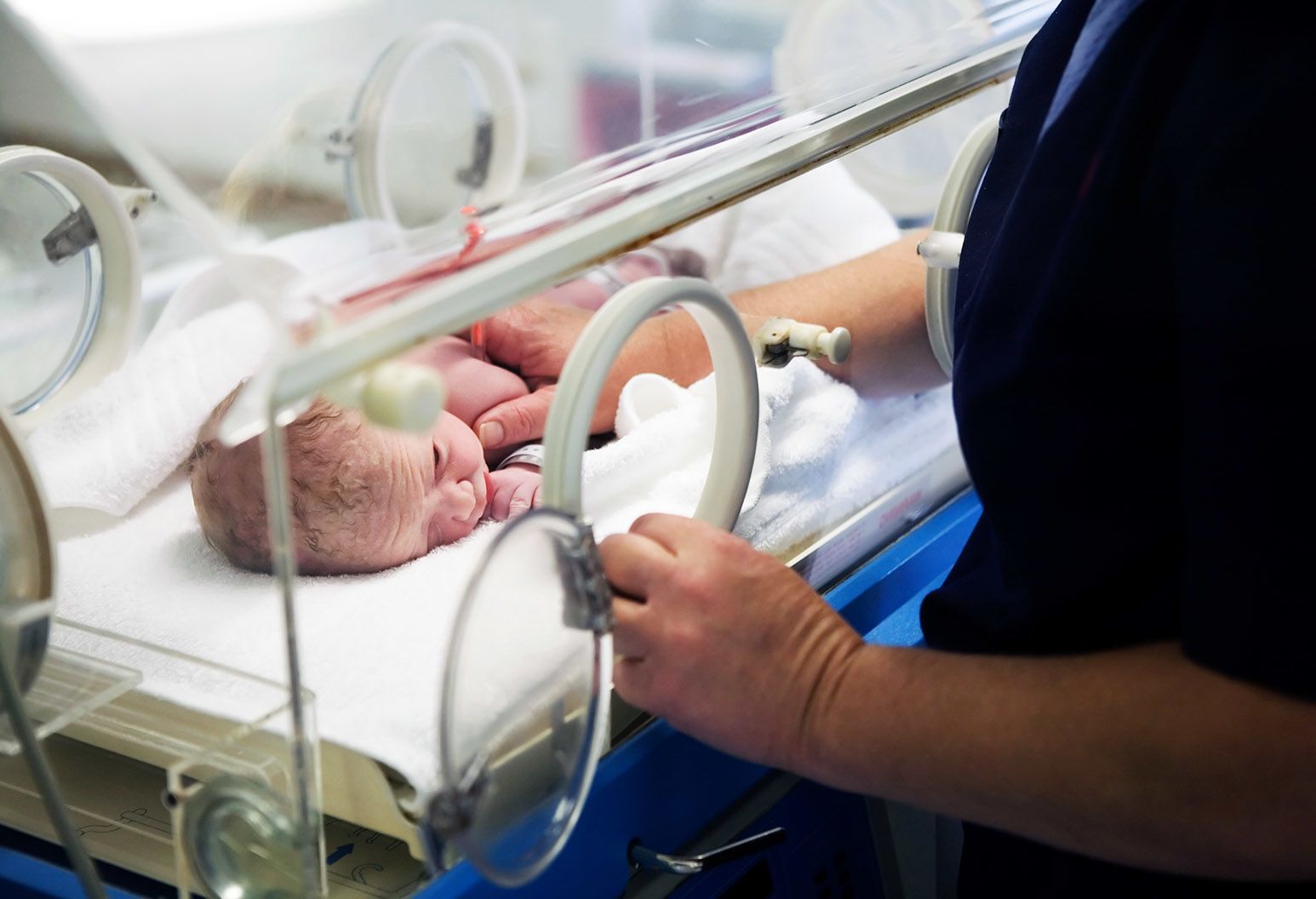 A female doctor with short blonde hair wearing green scrubs talks to the mother of a baby patient. The baby is on a scale in between them. The doctor is smiling.