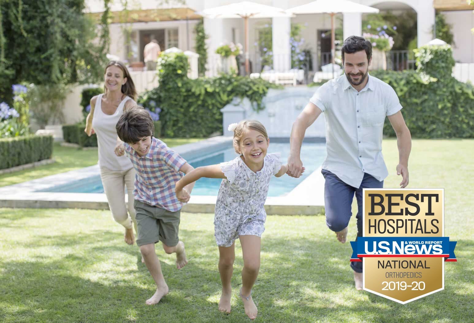 A mom, dad and two young kids hold hands and run together. They are in a backyard with a pool behind them. They're all barefoot and smiling.