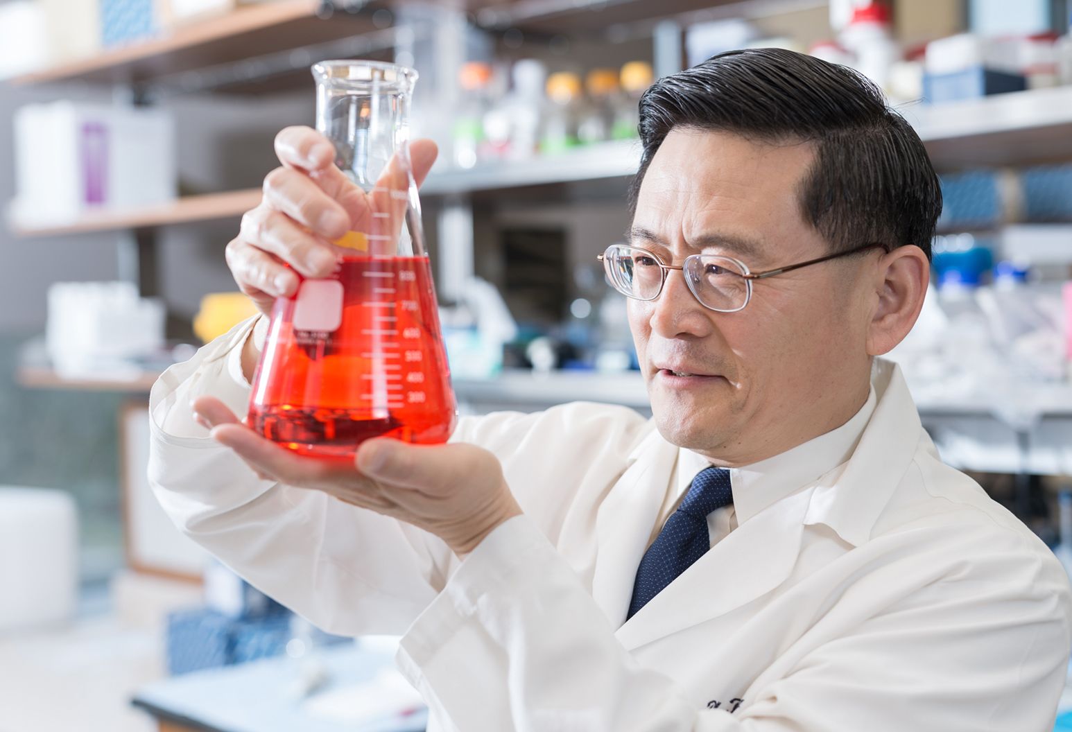 Researcher Ping Wang is examining a beaker with red liquid in it.