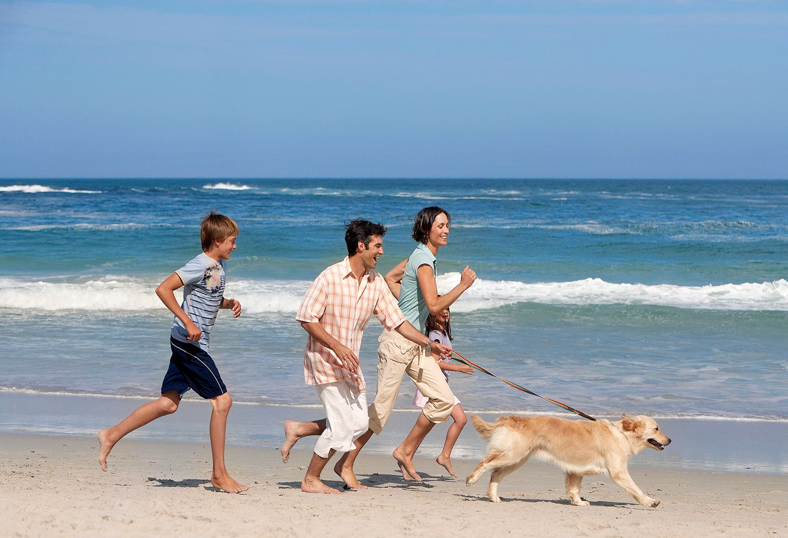 Family running on the beach with a dog