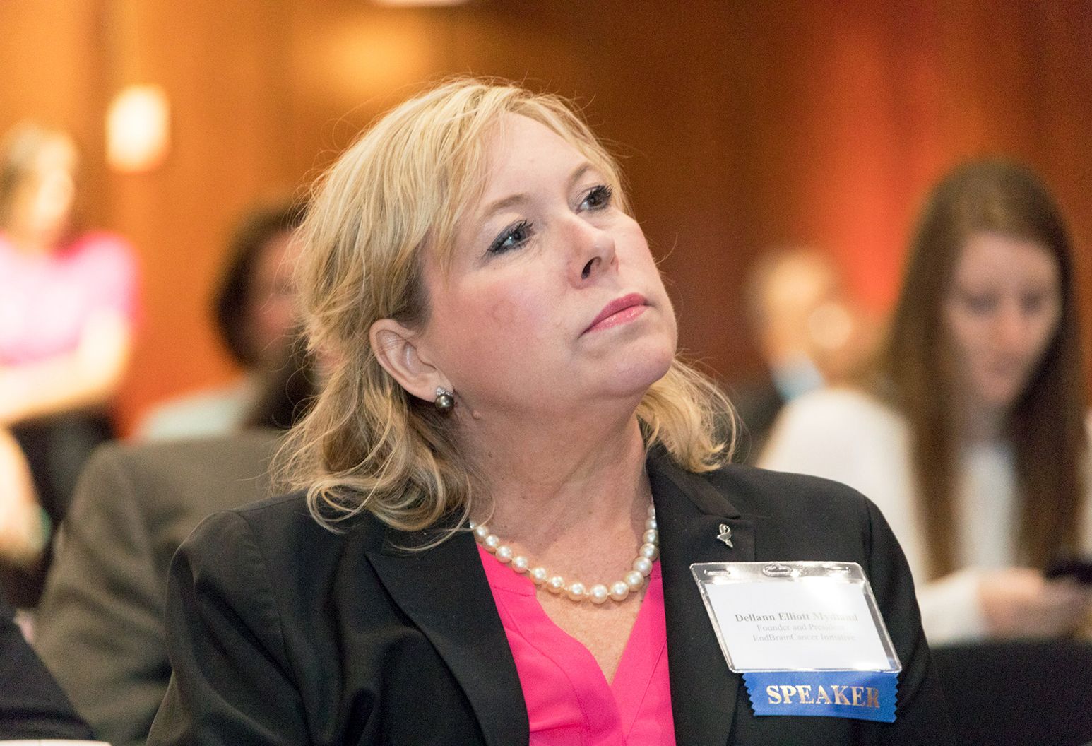 Middle aged woman wearing a suit is watching a presentation at a conference
