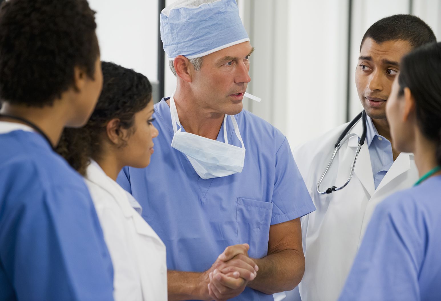 Five physicians, including residents, in scrubs and lab coats discussing the latest procedure.