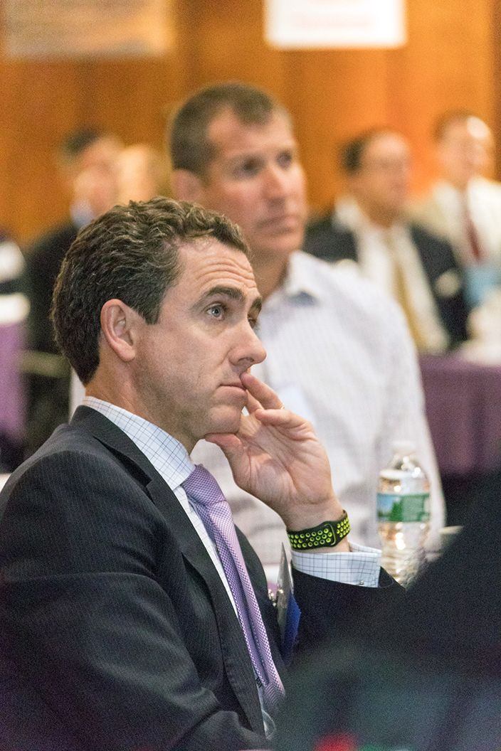 Middle aged man wearing a suit is watching a presentation at a conference
