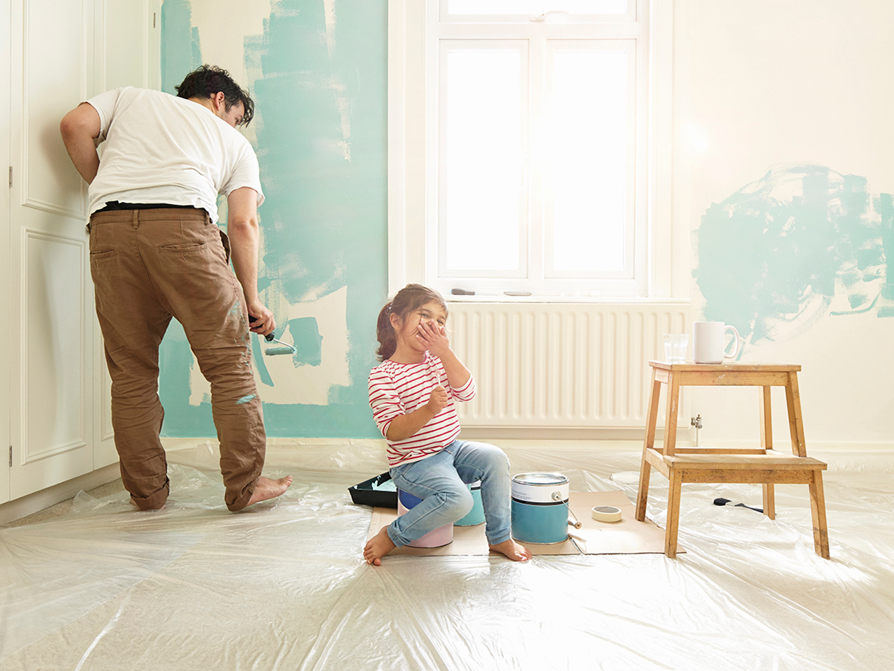 Daughter laughing while dad decorates wall in domestic home Daughter laughing while dad decorates wall in domestic home